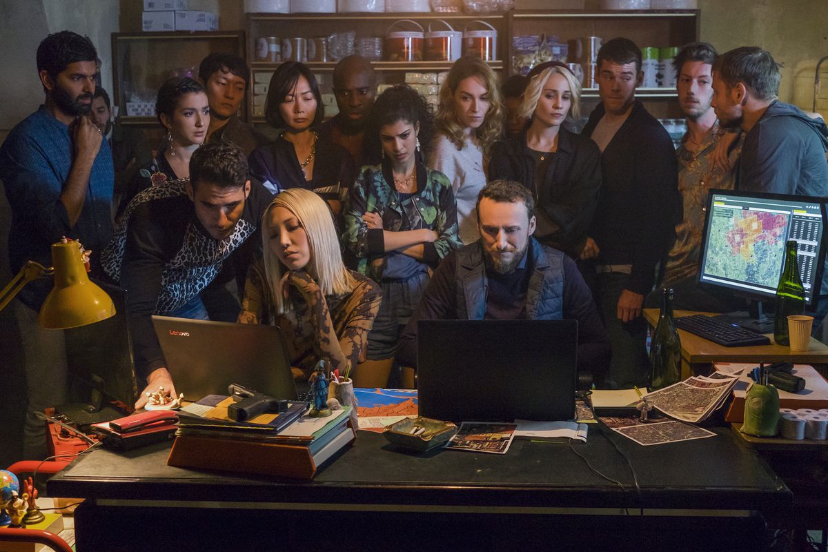A group of people, including the protagonists of Sense8, standing over the shoulders of two people typing on laptops in Sense8.