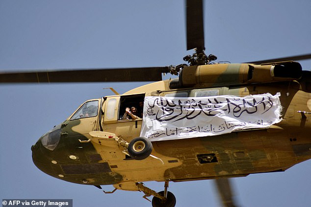 A helicopter with a Taliban flag flies above Taliban supporters who have gathered to celebrate the US withdrawal of all its troops from Afghanistan