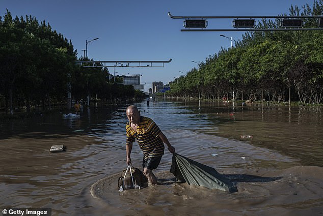 Scientists are increasingly linking extreme weather events to planetary warming, which is largely caused by CO2 emissions from fossil fuels.  For example, warmer air can hold more moisture, which means more intense rainfall and flooding.  Pictured, a man pulls a bag of goods recovered from a building as he wades through water on August 5, 2023 in Zhuozhou, Hebei province, south of Beijing, China