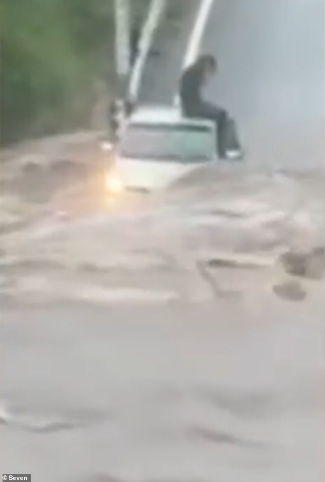 Images shared on social media showed a Queensland driver stranded and sitting on the roof of his car surrounded by floodwaters (pictured)