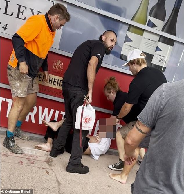 Dramatic footage shows a man being held outside a grocery store by a group of brave Good Samaritans (pictured)