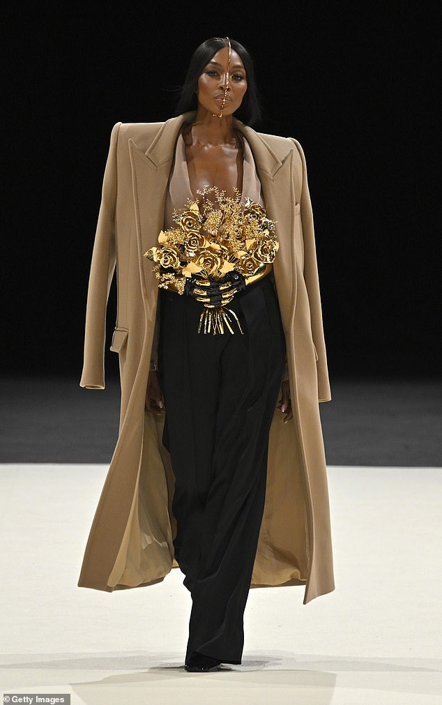 The supermodel wore a quirky gold headpiece that ran vertically down her face, as well as fake arms attached to her belt that held a metallic bouquet