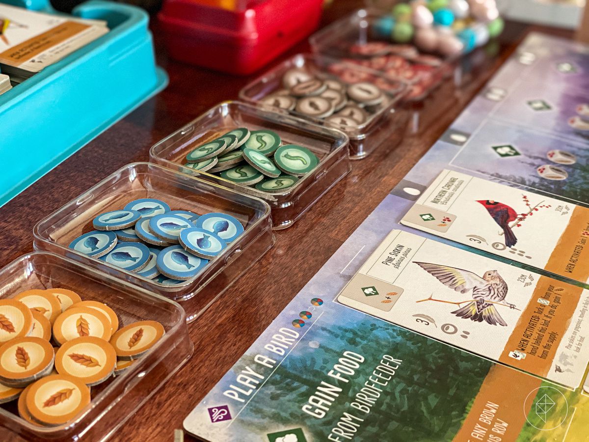 A selection of tokens in plastic containers, with cards filled with bird art along the sideboard.