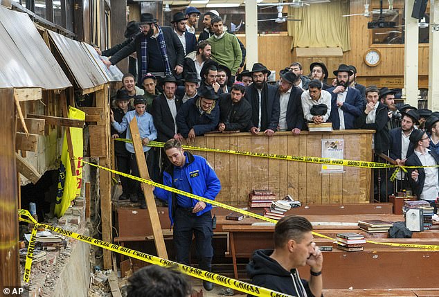 Hasidic Jewish students watch as police guard a broken wall in the synagogue on January 8