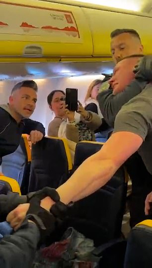 This is the shocking moment a holidaymaker was left in a standoff and forcibly marched off a Ryanair flight by police today after a flight from Luton to Lanzarote had to be diverted to Portugal due to his behaviour.