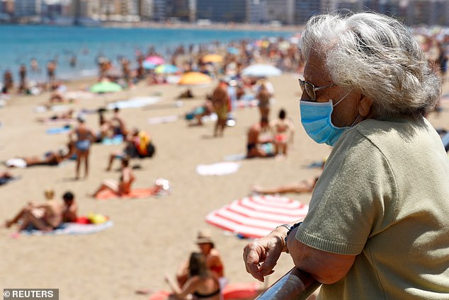 FILE PHOTO: A woman wearing a face mask looks at people sunbathing on the beach of Las Canteras in Las Palmas de Gran Canaria, Gran Canaria Island, Spain, May 31, 2020.