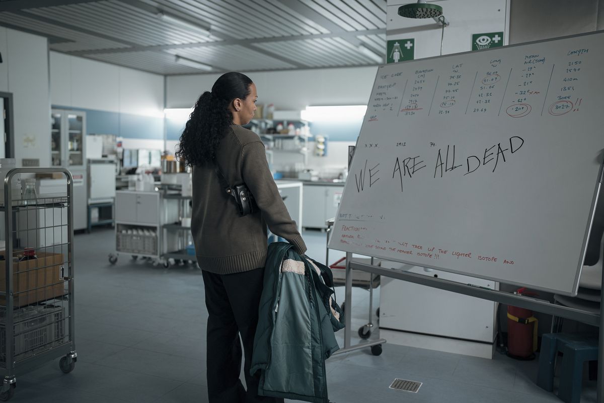 Kali Reis as Evangeline Navarro standing in front of a partially erased sign with the words 