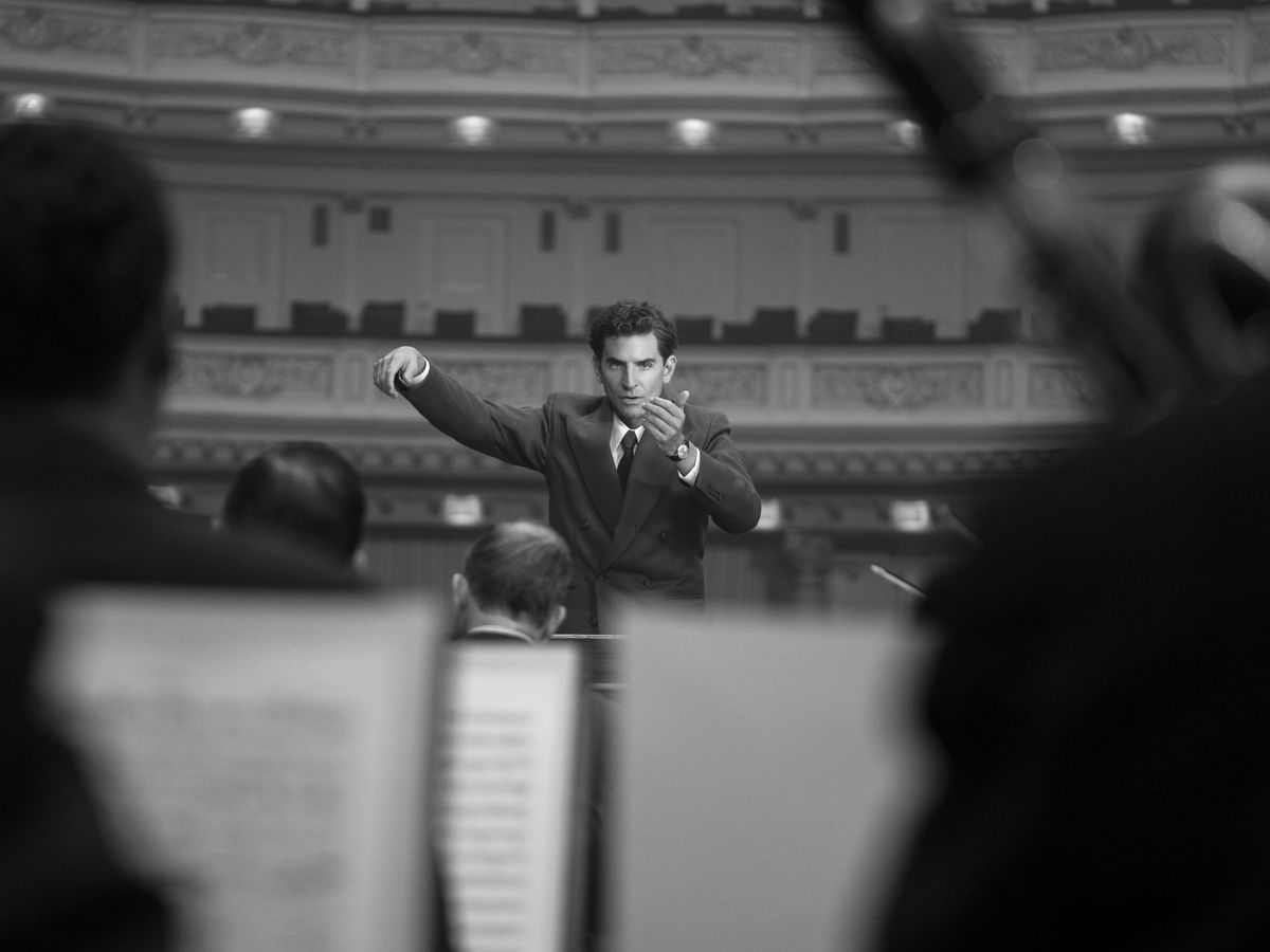 A man in a suit (Bradley Cooper) conducts a concert at Maestro.