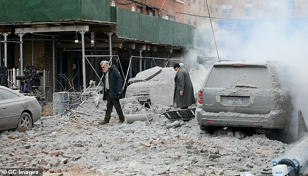 Colin and the colleague slowly walk through the rubble and smoke that has covered the cars on the set