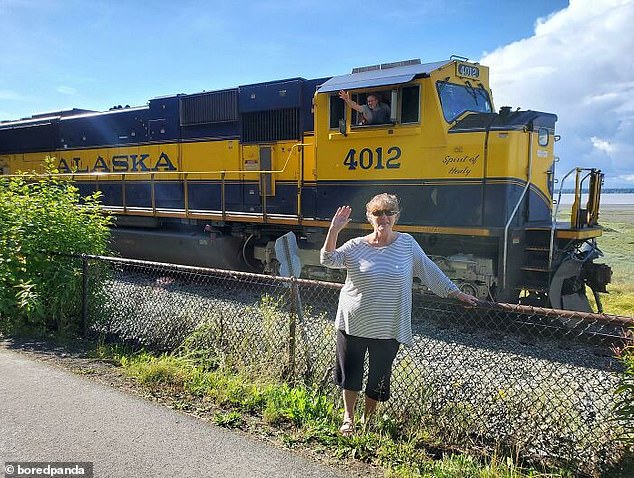 Fly past!  A train driver threw an arm out the window of his vehicle, which appeared to be in Alaska, as he drove behind a woman who briefly posed