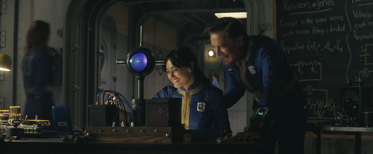 Lucy (Ella Purnell) and Hank (Kyle MacLachlan) sit in front of a gadget and laugh in a still from the Fallout TV series