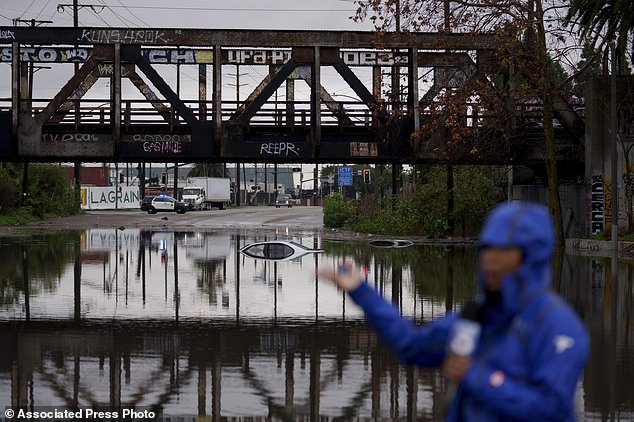 A television reporter does a broadcast in which cars are seen submerged in a flooded street under a railway bridge