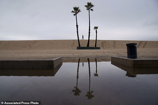 A person walks along the beach with flooding along the boardwalk in Seal Beach on Thursday