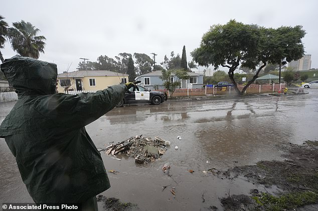 Ruben Gomez points along a partially flooded street as he breaks free from clearing mud and flood debris that engulfed his parents' home during the previous rainstorm, as more rain falls Thursday