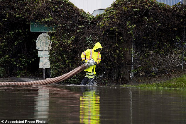 A worker carries a garden hose on a flooded street in Long Beach on Thursday