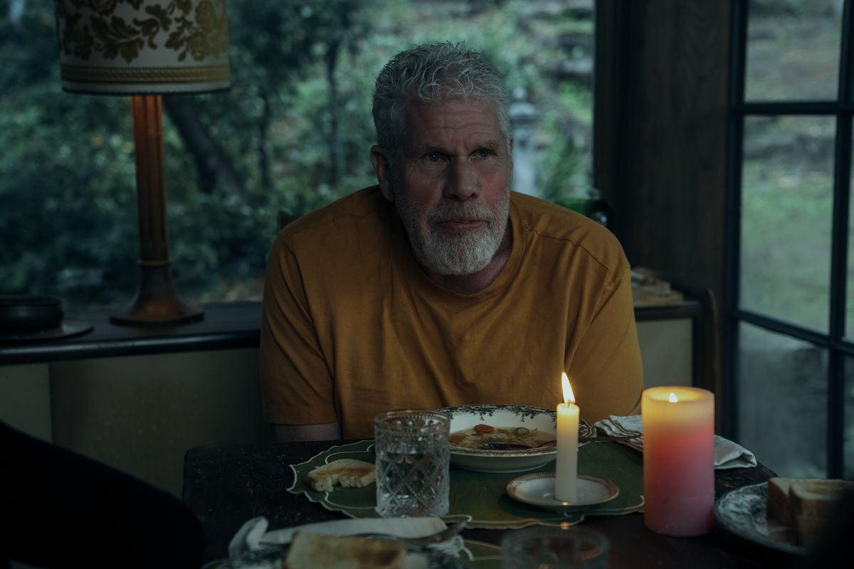 Ron Perlman looks sad in a yellow T-shirt at a candlelit dinner table at dusk in Mr.  & Mrs.  Smith