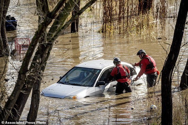 Search and rescue workers investigate a car surrounded by floodwaters