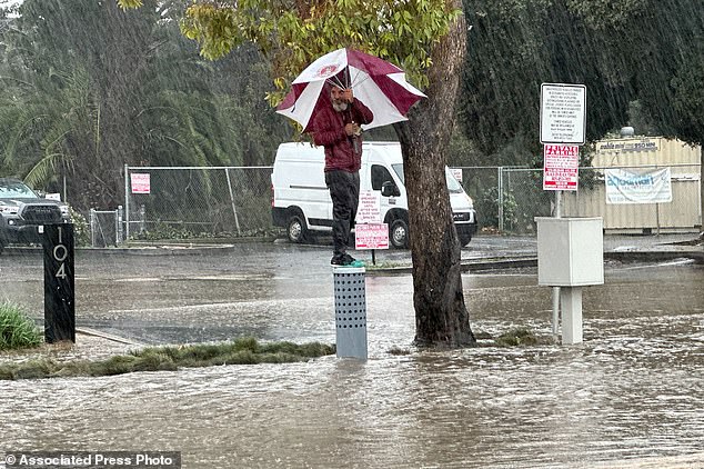 A man with an umbrella stands high above a flooded street in Ventura