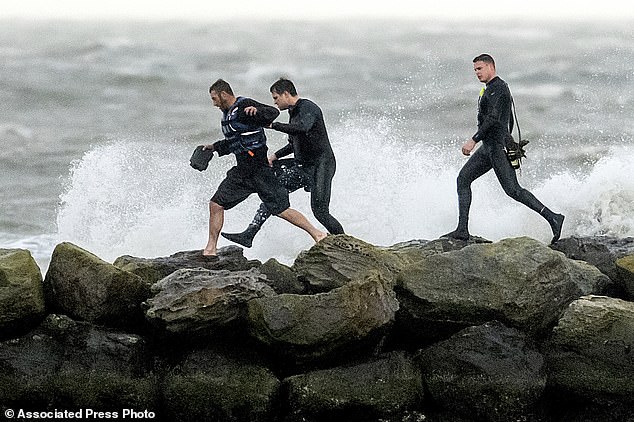 Rescuers assist a boater, left, after his sailboat drifted toward a breakwater while dragging anchor