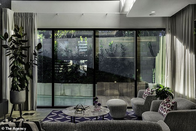 A cozy lounge sits beneath a two-story loft with windows that reach all the way to the ceiling, letting in natural light, while a home study is hidden behind the TV wall