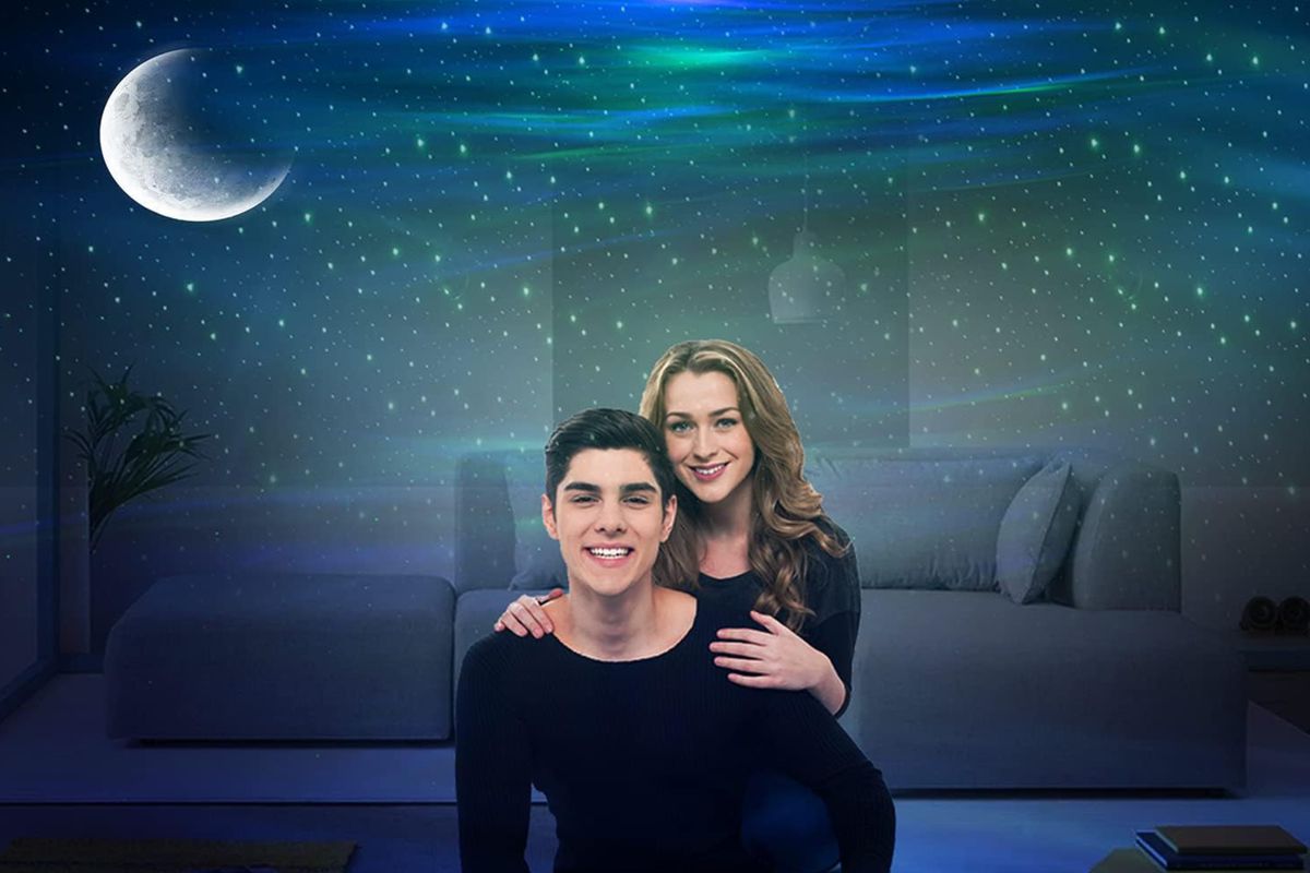 An image of two people in a gentle embrace in a room where the Cadrim star projector projects colors and images of stars and the moon onto their walls and ceiling.