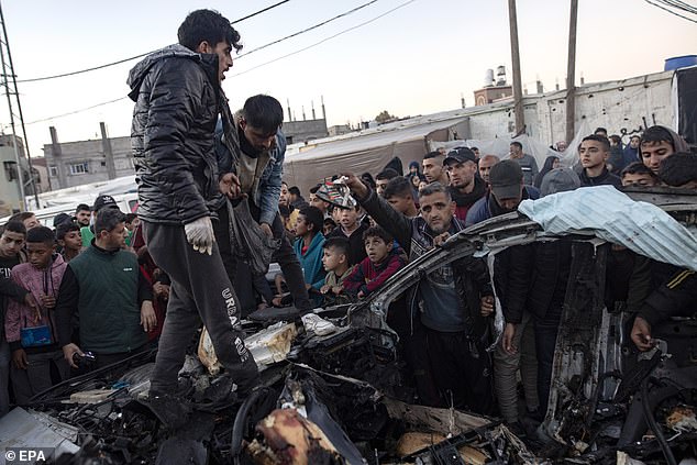 Palestinians jump into a burnt-out car in Rafah amid the conflict