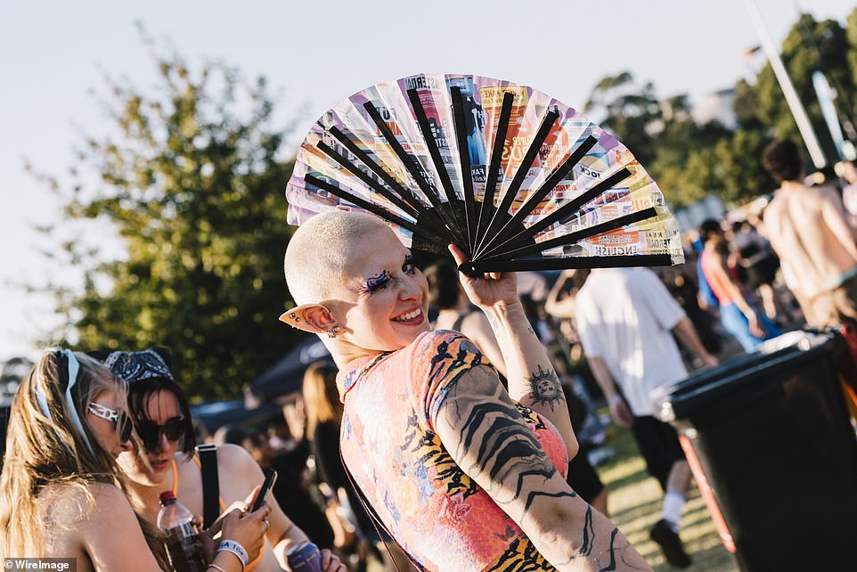 The photo shows a tattooed festival goer who accessorized his festival look with prosthetic elf ears, light makeup and a portable fan