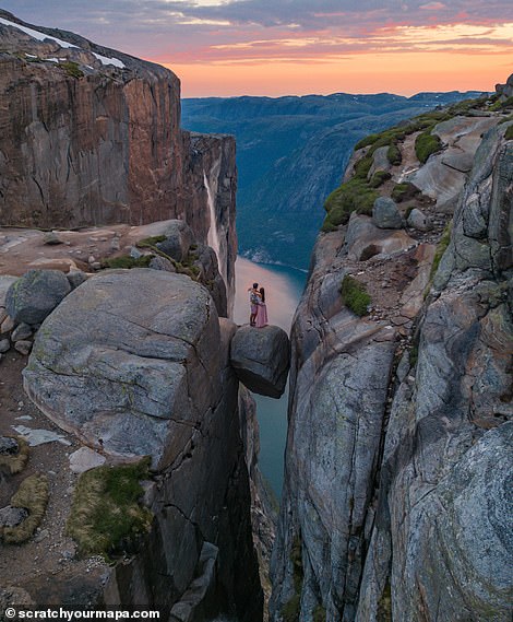 Danni and Fede stand on Kjeragbolten, a boulder stuck in a crevice 984 meters above sea level on Kjerag Mountain in Norway's Lysefjord.  The popular tourist destination can be reached without hiking equipment