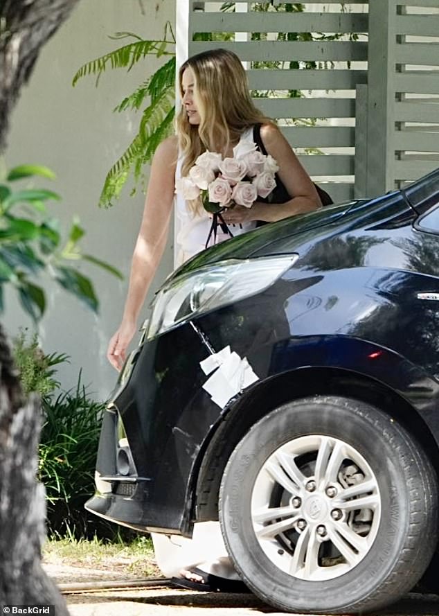 Margot had her hands full with a bouquet of flowers and a pink gift bag and looked excited as she walked to the front door to greet her beloved mother