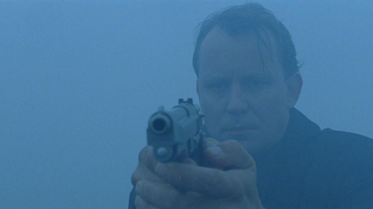 A medium shot of a man holding a gun, surrounded by fog.