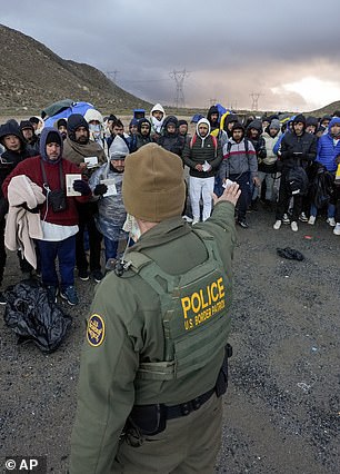 A Border Patrol agent asks asylum-seeking migrants to line up at a makeshift, mountainous campsite