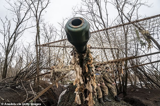 Ukrainian soldiers deploy a camouflaged net over a military vehicle in their fighting position near Bakhmut