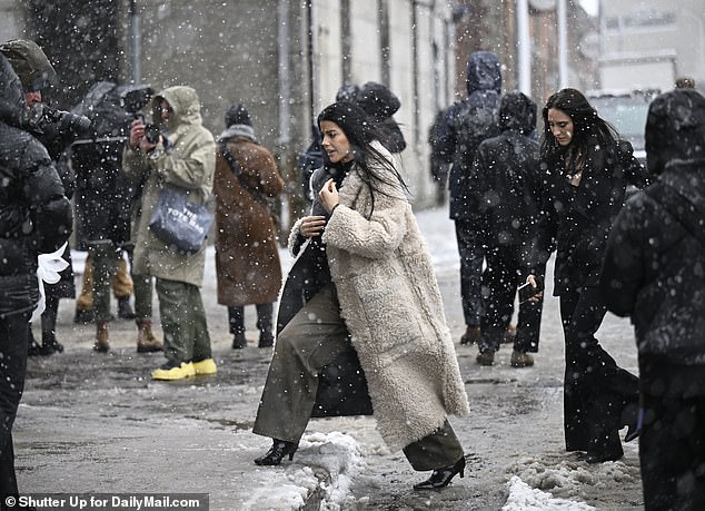 A fashionista, wearing a fluffy brown coat and heeled boots, steps over piles of snow to the Gabriela Hearst Fashion Show