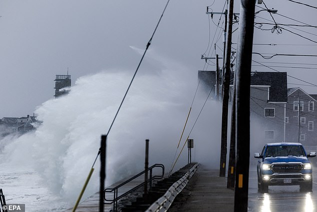 A car drives by as waves crash over the seawall in Marshfield, Massachusetts, on Tuesday