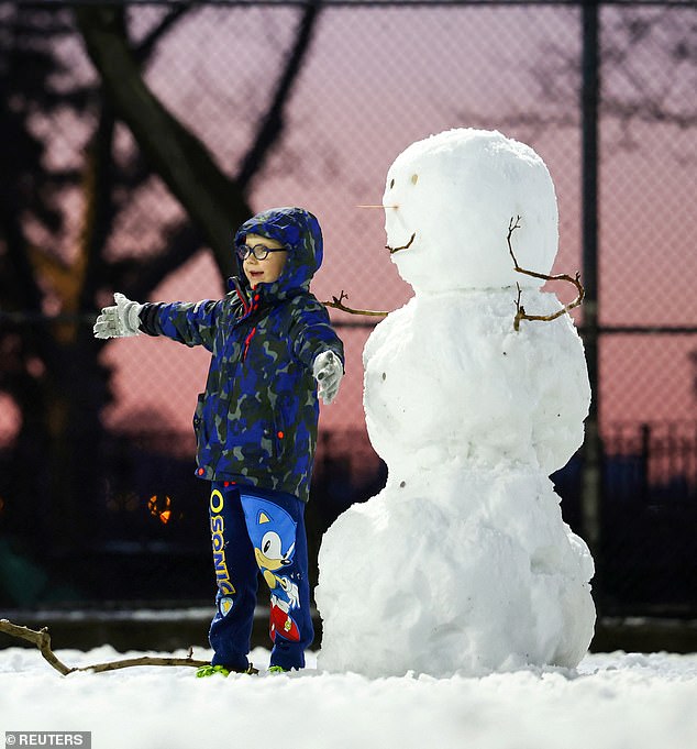 A child poses with a snowman after a winter storm in New York City's Nor'easter