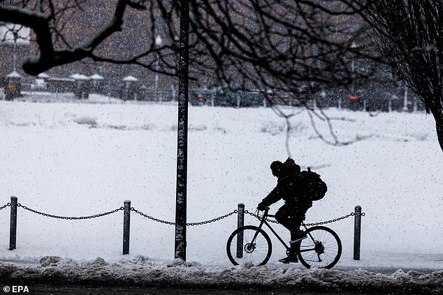 A passerby rides a bicycle on a snow-covered sidewalk in Providence, Rhode Island, on Tuesday