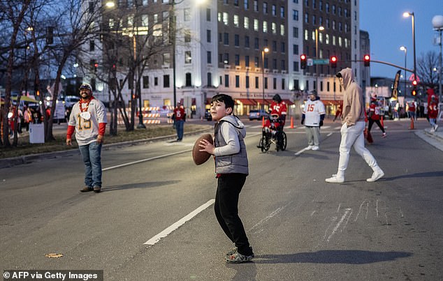 A young fan throws a football in the closed street while the sun is still rising