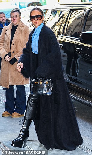 The 54-year-old singer showed off a stylish look in a bright blue button-up blouse, paired with a fitted faux leather midi skirt and a long, cozy trench coat