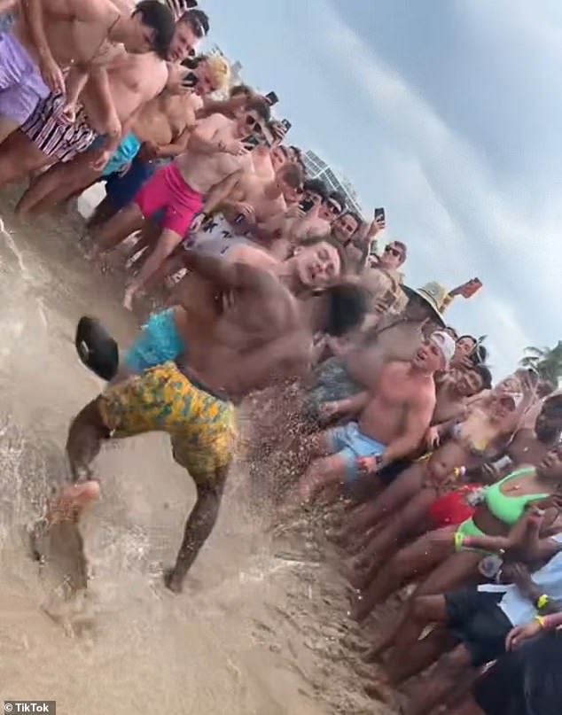 Two cheerful students celebrating a break from their college semester took turns jumping on each other and fighting as the crowd around them cheered and shouted