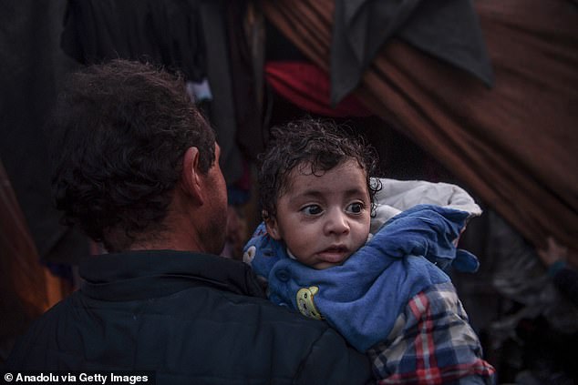 A Palestinian man is seen with his baby in front of the makeshift tents on Saturday as Palestinian families who left their homes and sought shelter in the city of Rafah protect themselves from Israeli attacks