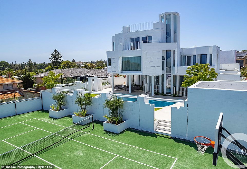 At the very back of the building there is a tennis court and basketball hoop, surrounded by a large white brick wall