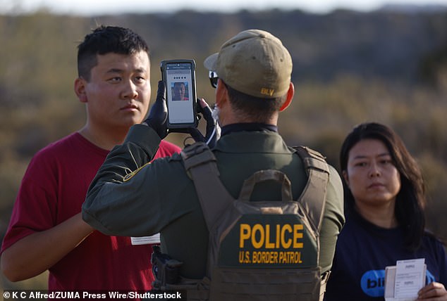 An asylum-seeking migrant from China holds up his passport and paperwork as he is photographed by a U.S. Border Patrol in December 2023