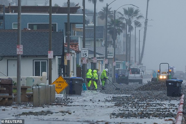 Work crews clear a beach road Tuesday after ocean waves caused by a winter storm pushed up beach cliffs in Oceanside, California