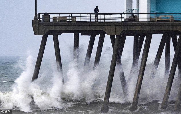 Waves crash against the pilings of the Huntington Beach Pier in Huntington Beach as another storm brings rough surf, rain, wind and cool temperatures to Southern California