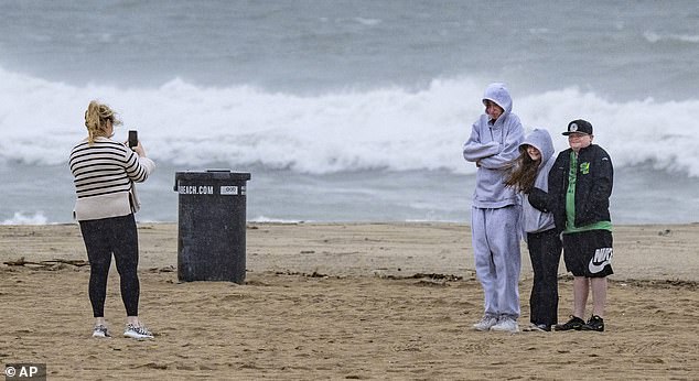 Visitors pose for a photo south of the Huntington Beach Pier as a storm brought high winds, rain and rough surf to the beach