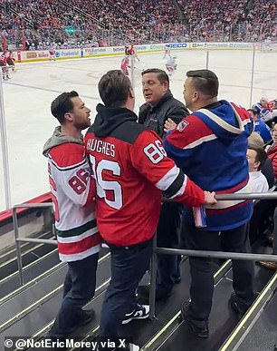 The Devils fan, wearing a replica Jack Hughes No. 86 jersey, is seen arguing with another man in a winter coat along a staircase in one of the lower areas of the Prudential Center