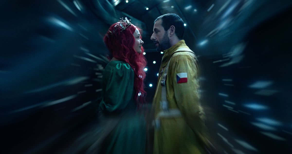 Lenka (Carey Mulligan, in a silver tiara, flowing red wig and green ball gown) stands close to Jakub (Adam Sandler), dressed as an astronaut in a yellow flight suit, as everything around them fades away in a scene from Netflix's Spaceman