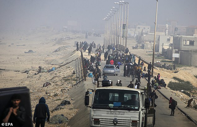 Dust and smoke from airstrikes engulf Palestinians walking along Al Rashid Road after crossing from the northern Gaza Strip to southern Gaza City