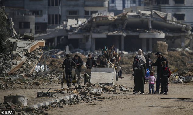 Palestinians walk past destroyed houses in the Al Nusairat refugee camp