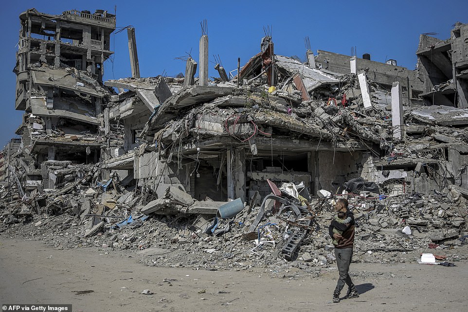 A Palestinian man carries a baby past buildings destroyed during Israeli attacks in Beit Lahia in northern Gaza